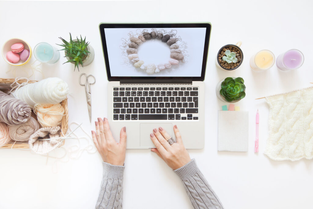 A woman knits, edits an online store on a laptop. Work at home.